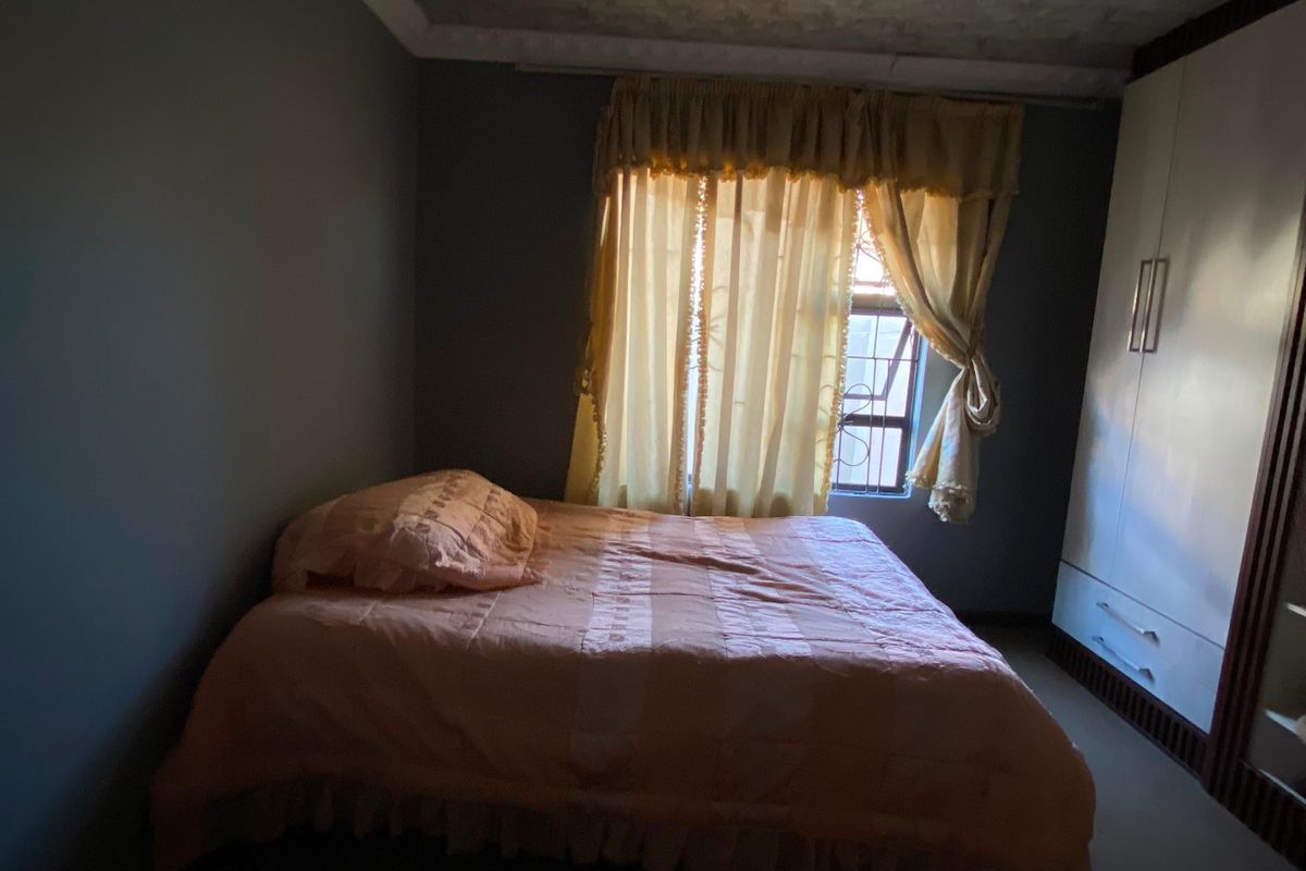 A bedroom featuring a built-in wardrobe, decorative ceiling molding, and security bars on the window. The room requires cosmetic updates to improve its appeal.