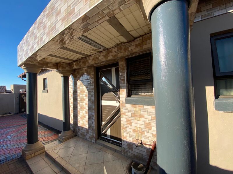 Front entrance area featuring a covered porch with decorative columns, tiled facade cladding, and a secure entrance door.