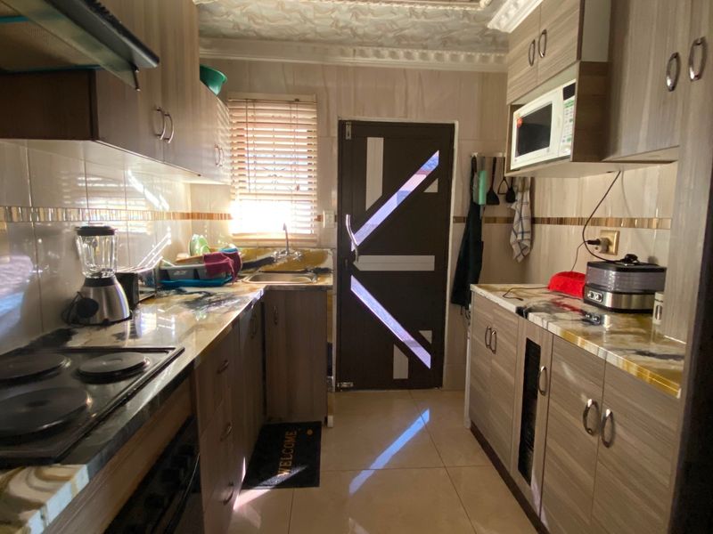 A functional galley-style kitchen featuring wood-grain cabinetry, integrated appliances, tiled surfaces, and a unique decorative ceiling finish.