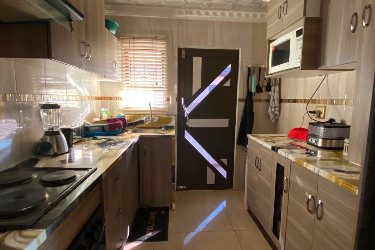 A functional galley-style kitchen featuring wood-grain cabinetry, integrated appliances, tiled surfaces, and a unique decorative ceiling finish.