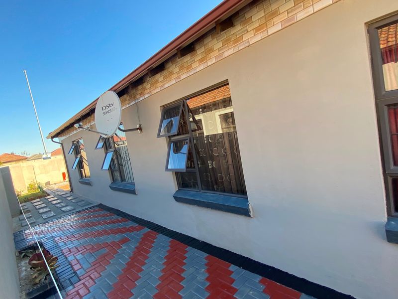Side view of the property featuring a clean rendered facade, top-hung windows, and neatly laid patterned brick paving.