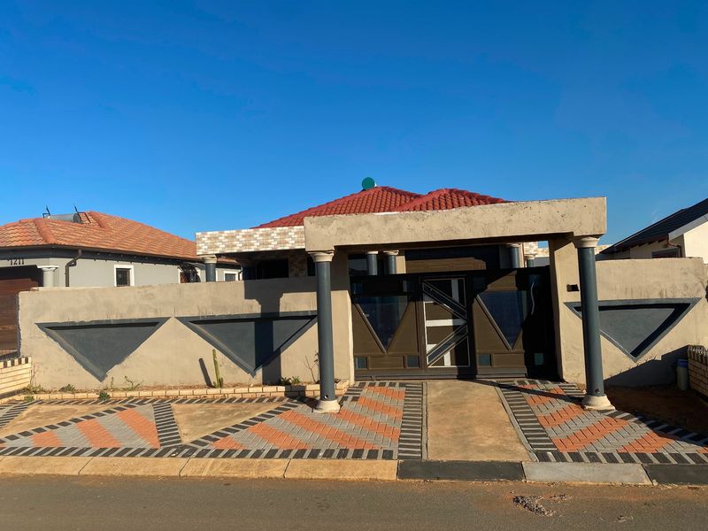 Front elevation of a residential property featuring a gated entrance, perimeter wall with decorative accents, and a paved driveway.
