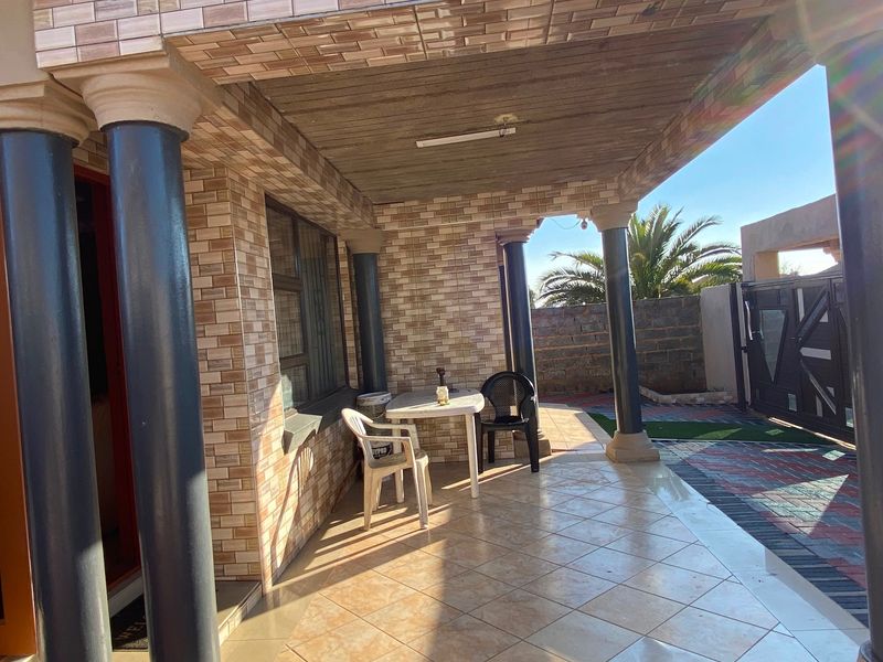 A covered patio area featuring decorative brick cladding, structural columns, and tiled flooring, providing a functional outdoor space for relaxation.