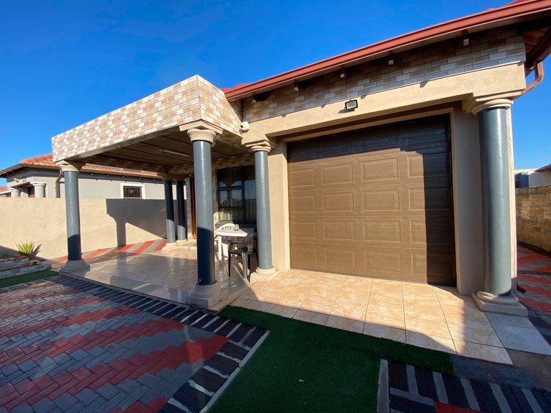 Front view of the house featuring a covered tiled patio with decorative columns, a paved driveway, and a secure sectional garage door.