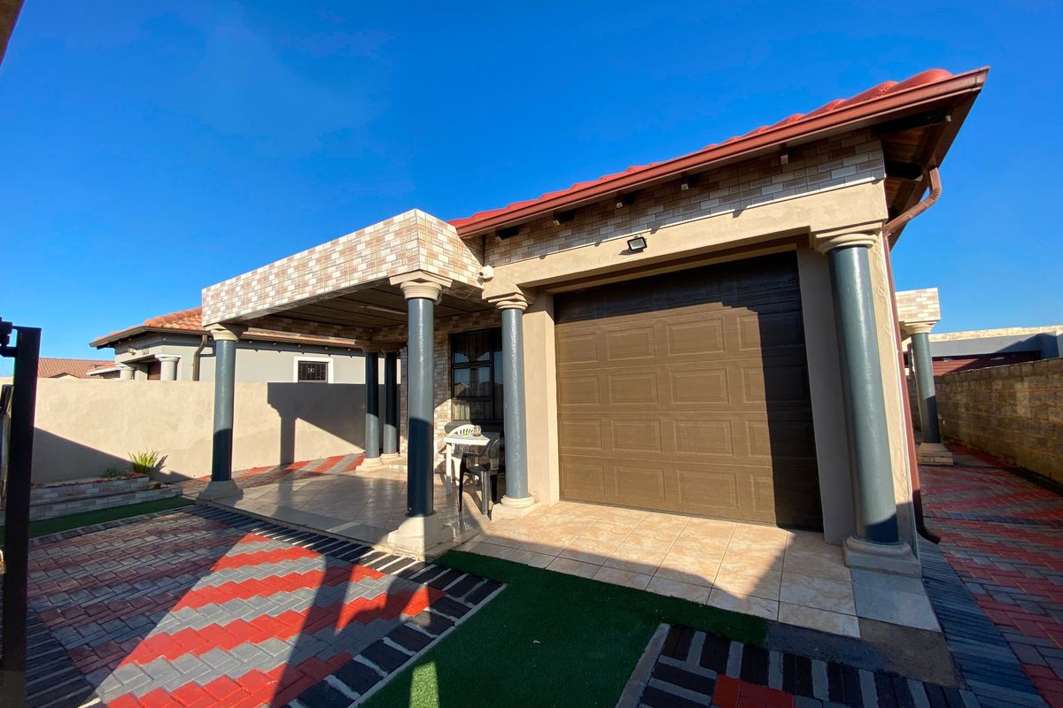 A well-maintained rear exterior view featuring a covered patio with decorative columns, a tiled roof, and a paved outdoor area.
