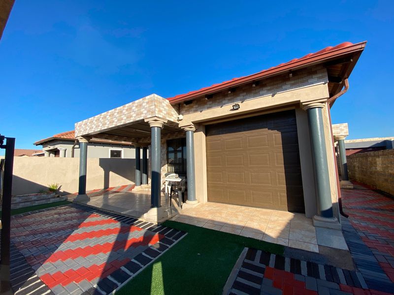 A well-maintained rear exterior view featuring a covered patio with decorative columns, a tiled roof, and a paved outdoor area.