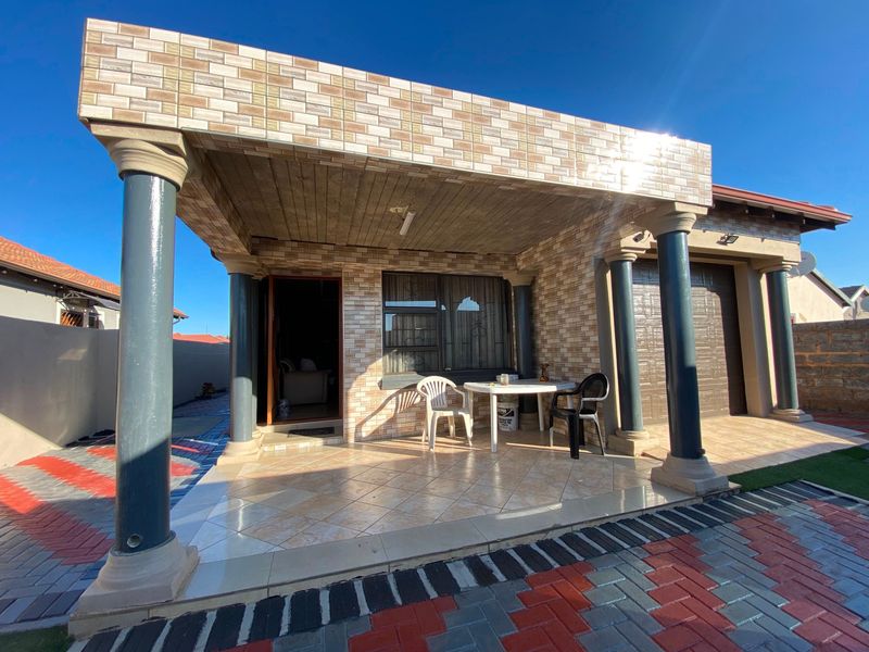 A covered patio area featuring decorative stone cladding, structural columns, and tiled flooring, providing a functional outdoor space adjacent to the main entrance.