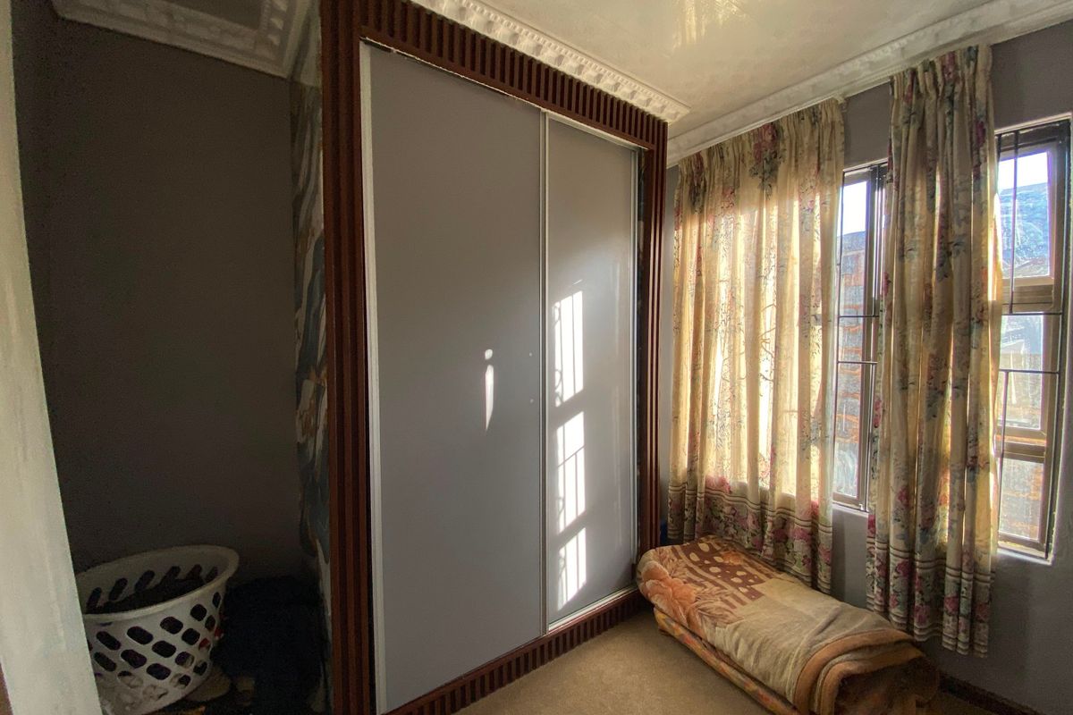 A bedroom featuring a large built-in wardrobe with dark wood trim, decorative ceiling cornices, and natural light through a window.