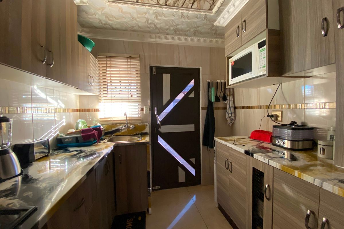 A functional kitchen featuring wood-look cabinetry, stone-effect countertops, a built-in microwave, and decorative ceiling detailing with integrated lighting.