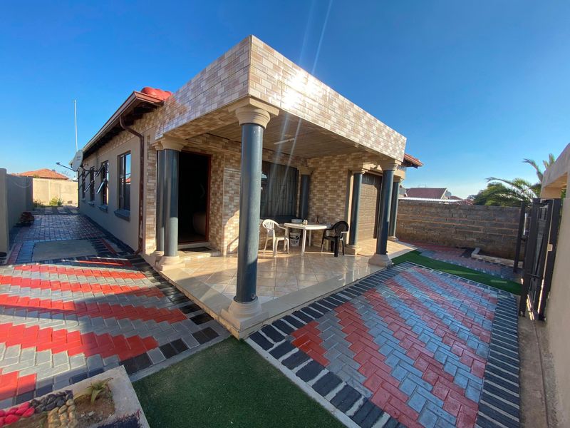 A well-maintained front exterior featuring a covered tiled patio with decorative columns and extensive brick-paved driveway and courtyard area.