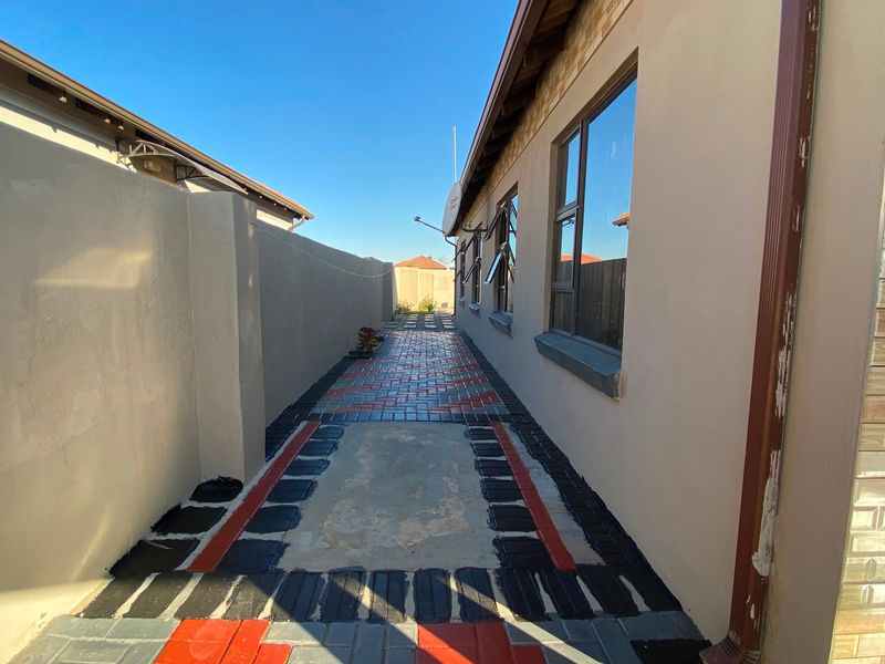 A side passage featuring a paved walkway between the house exterior and a high boundary wall, with aluminium window frames and a downpipe.