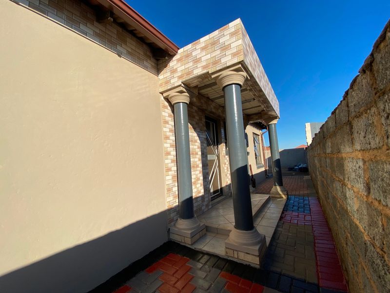 A side exterior view of the property featuring a covered patio area with decorative columns, brick cladding, and paved outdoor flooring.