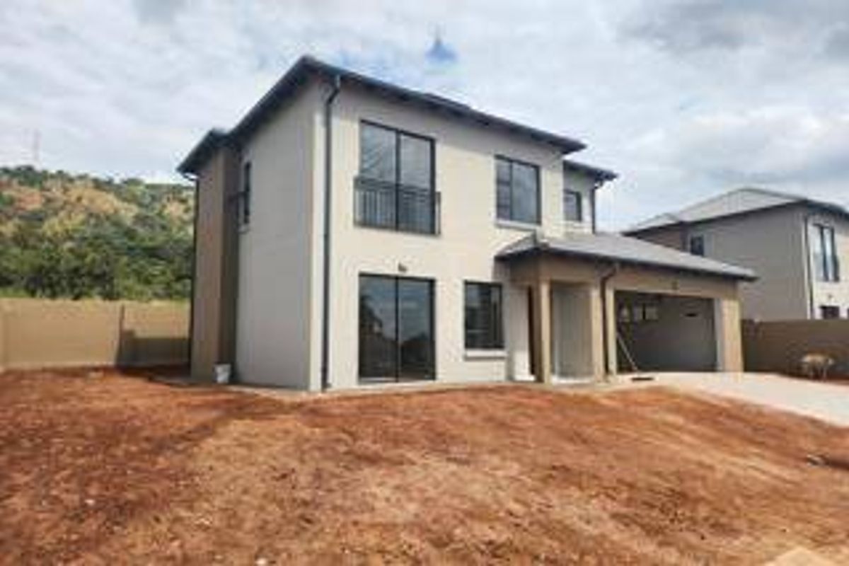 A modern double-storey residential property featuring a rear facade with sliding doors, a balcony, and an attached garage, set on an unlandscaped plot.