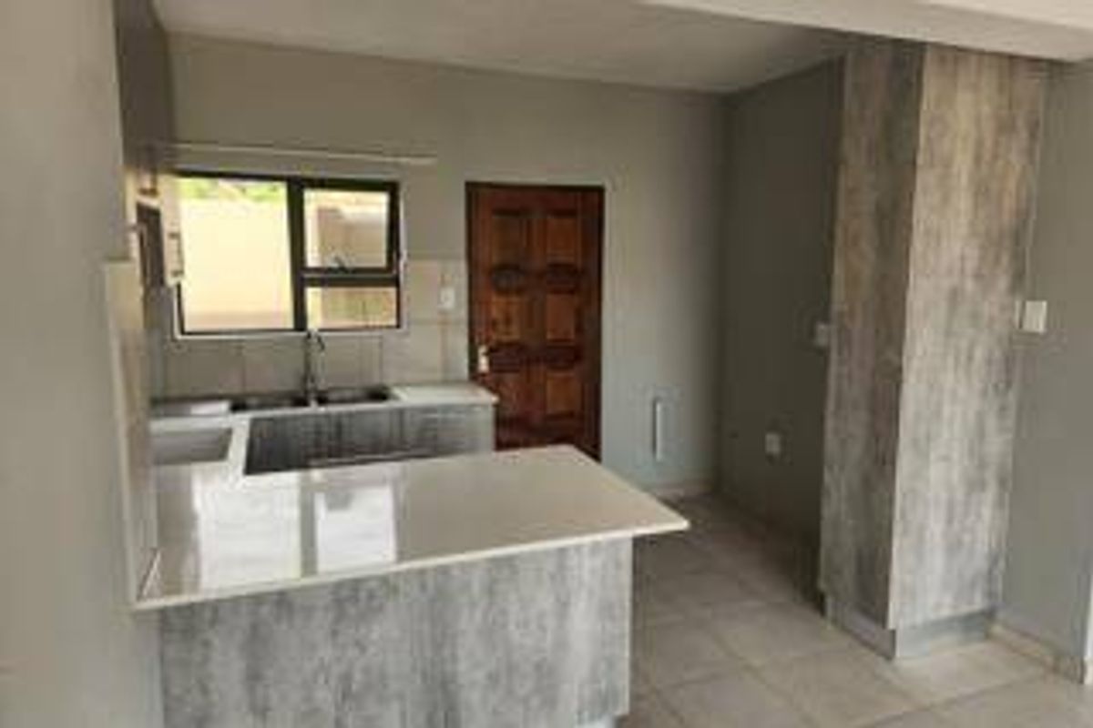 A clean, modern kitchen featuring stone countertops, grey laminate cabinetry, and tiled flooring, offering a functional and neutral space ready for personalization.