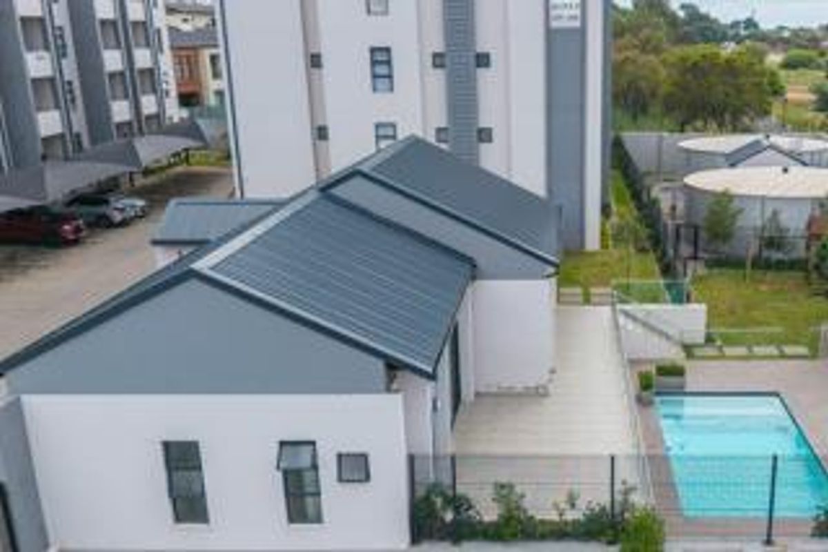 Aerial view of a townhouse complex featuring a modern metal roof, private swimming pool, paved patio area, and secure perimeter fencing.