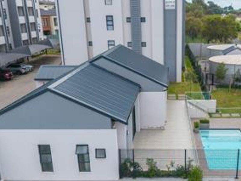 Aerial view of a townhouse complex featuring a modern metal roof, private swimming pool, paved patio area, and secure perimeter fencing.