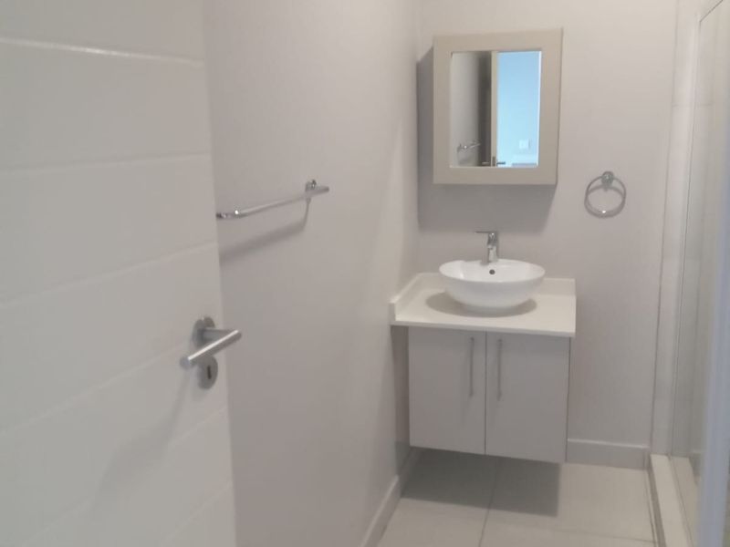 A clean, modern bathroom featuring a floating vanity with a vessel sink, a wall-mounted mirror, and a glass-enclosed shower.