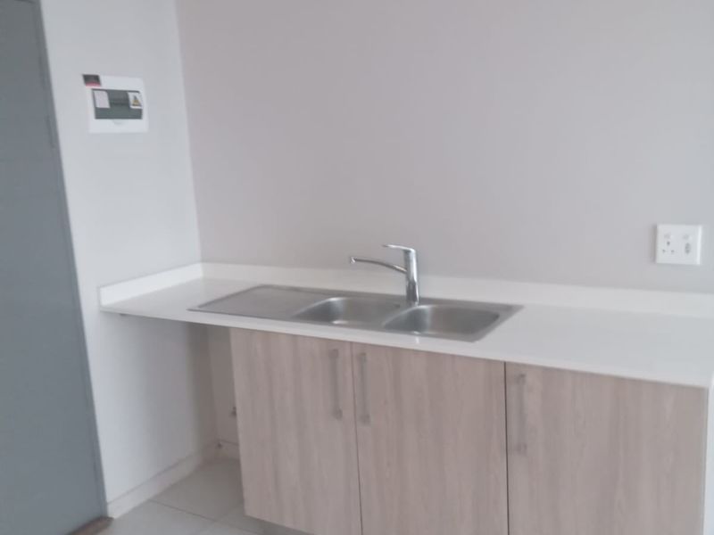 A clean and functional scullery area featuring modern laminate cabinetry, a stainless steel sink with a mixer tap, and neutral tiled flooring.