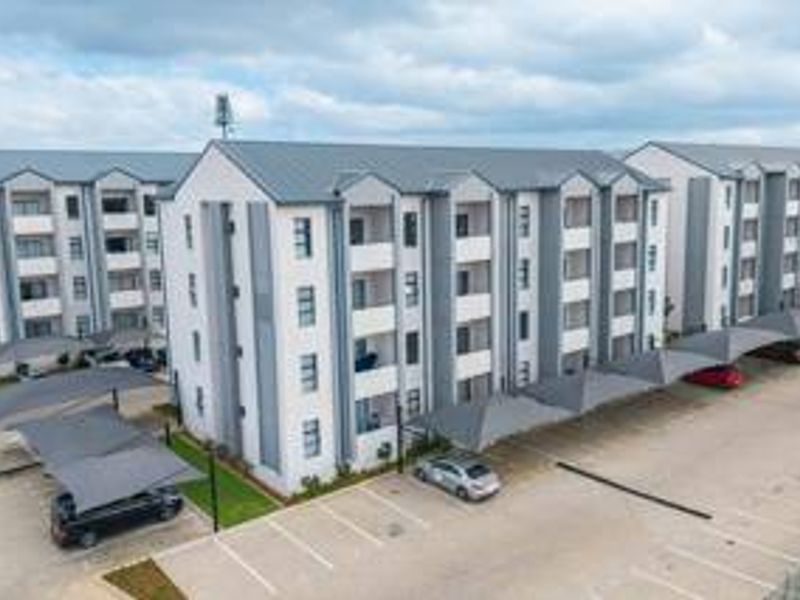 Aerial view of a modern multi-story townhouse complex featuring a metal roof, paved parking area, and covered parking bays.