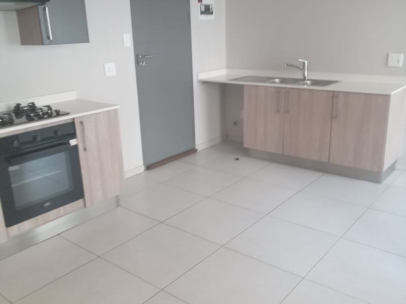 A clean, modern kitchen featuring light wood cabinetry, stone countertops, a built-in oven with gas hob, and neutral tiled flooring.