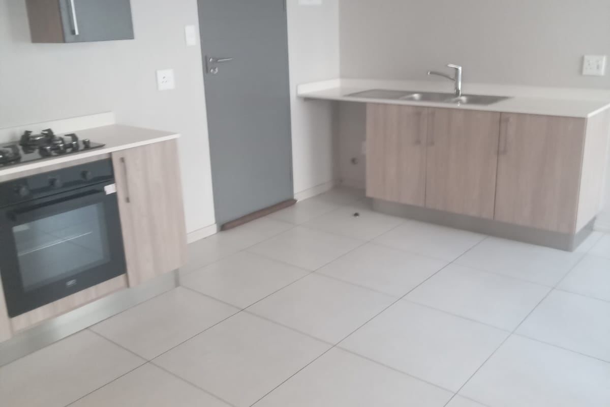A clean, modern kitchen featuring light wood cabinetry, stone countertops, a built-in oven with gas hob, and neutral tiled flooring.