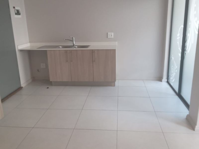 A clean, empty scullery or utility area featuring modern light wood cabinetry, a stainless steel sink, and neutral tiled flooring with access to the outdoors.
