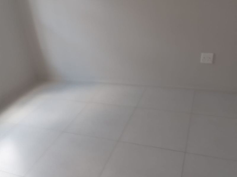 An empty bedroom featuring neutral tiled flooring and a clean wall finish, providing a blank canvas for interior design.