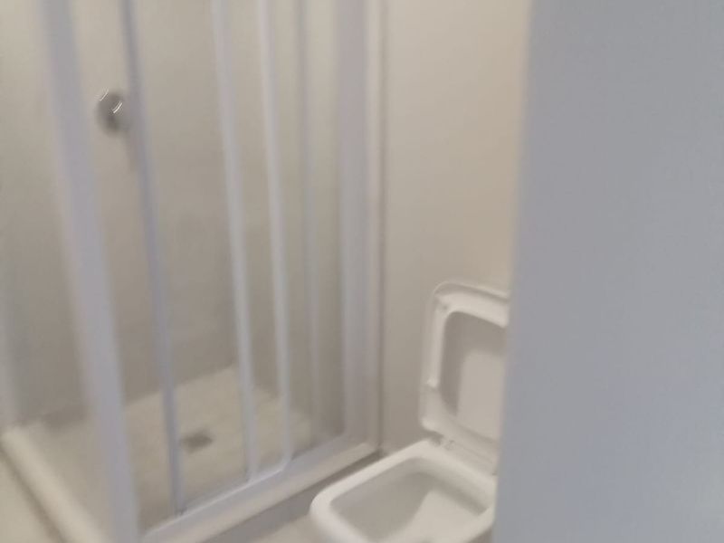 A compact bathroom featuring a white toilet and a separate shower enclosure with tiled flooring.
