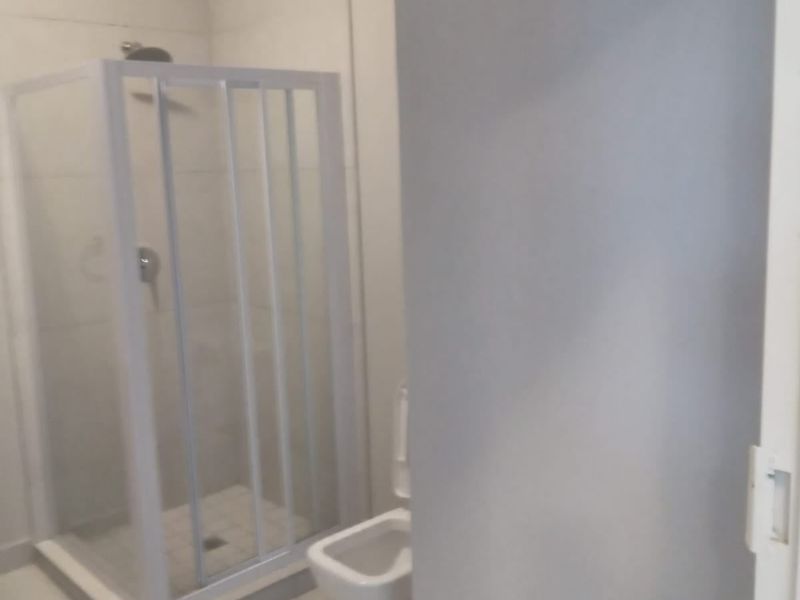 A clean, functional bathroom featuring a glass-enclosed shower and a standard toilet with neutral tiled finishes.
