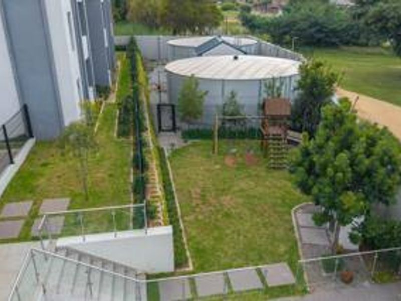 Aerial view of the rear garden area featuring landscaped lawn, paved pathways, glass balustrades, and large water storage tanks at the rear boundary.
