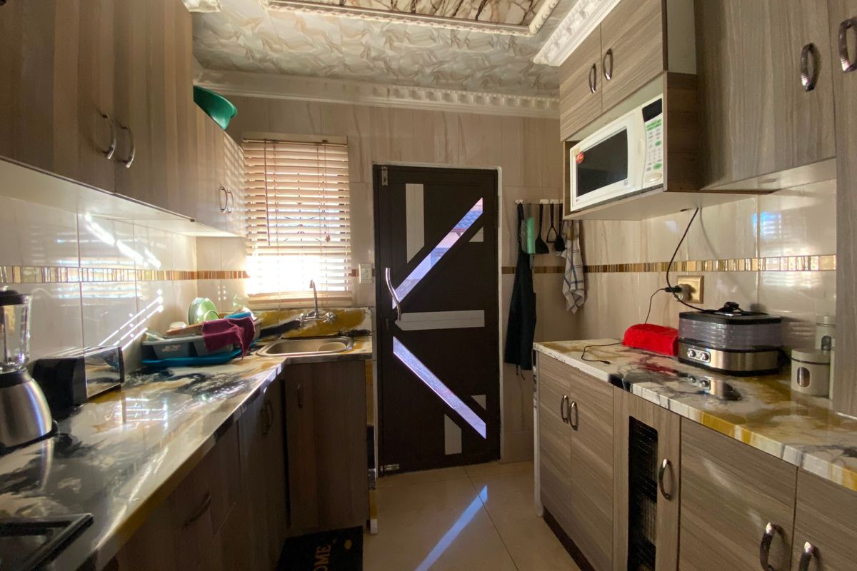 Compact kitchen featuring wood-grain cabinetry, marble-effect countertops, tiled backsplash, and built-in microwave, offering a functional layout with direct exterior access.