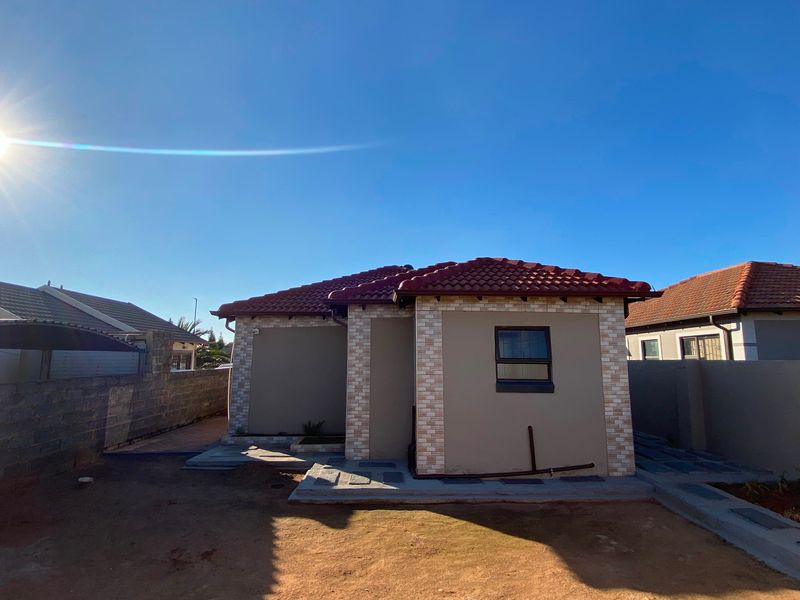 Rear view of the property featuring a tiled roof, brick-accented facade, and concrete paving, set within a walled perimeter.