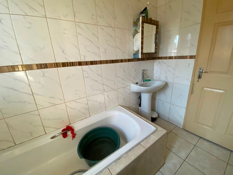 A functional bathroom featuring a built-in bathtub, pedestal basin, and tiled wall finishes, offering a blank canvas for potential modernization and renovation.