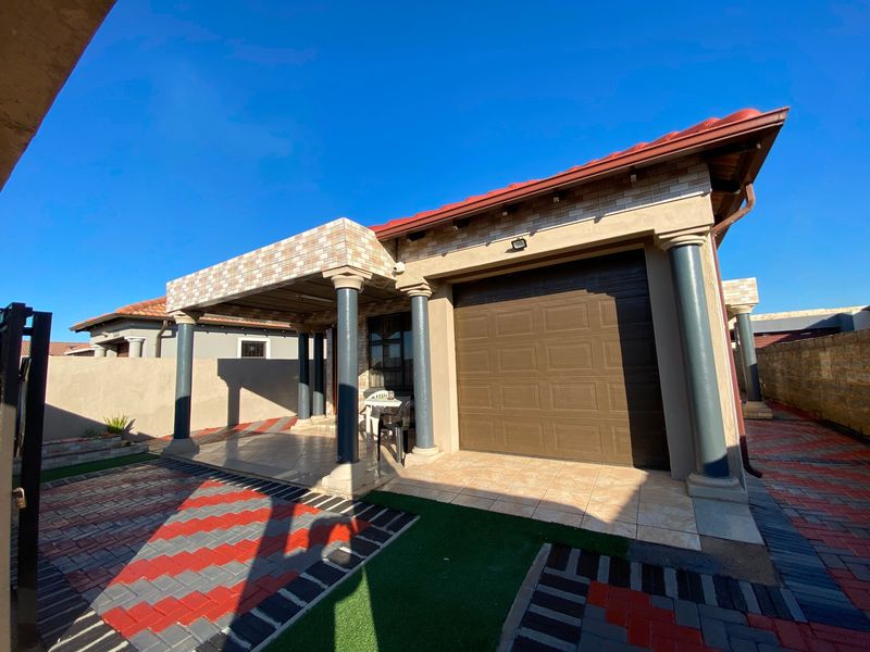 A well-maintained front exterior featuring a covered patio, decorative columns, an automated garage door, and a neatly paved driveway with artificial grass accents.