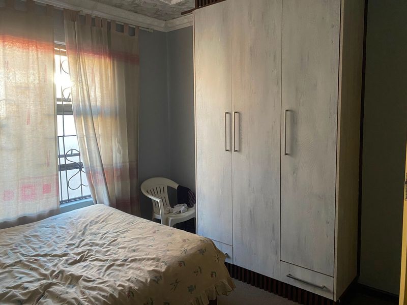 A bedroom featuring a large built-in wardrobe with modern handles and a window fitted with security bars.