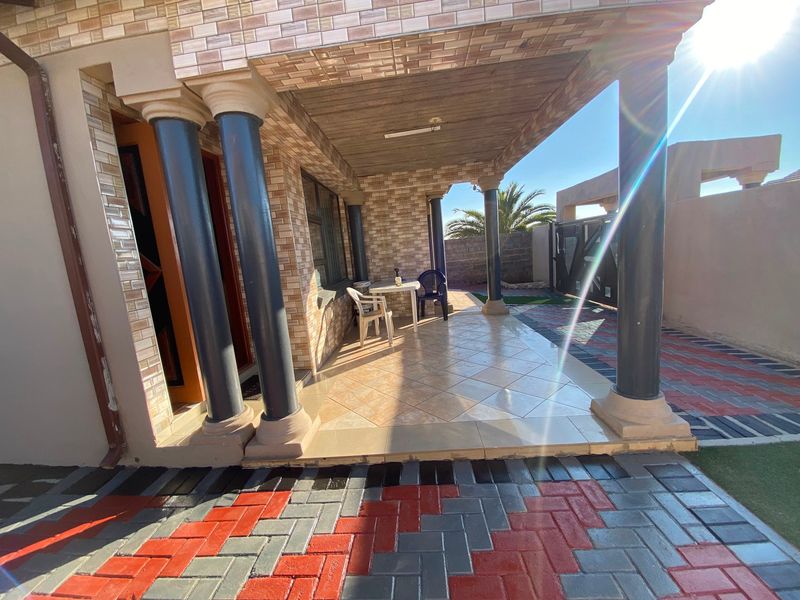 A covered patio area featuring decorative columns, tiled flooring, and brick-style wall cladding, overlooking a paved outdoor space.