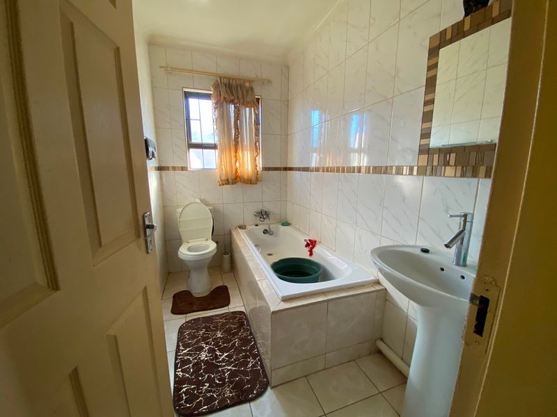A functional bathroom featuring a pedestal basin, built-in bathtub, and toilet, finished with neutral wall and floor tiles.