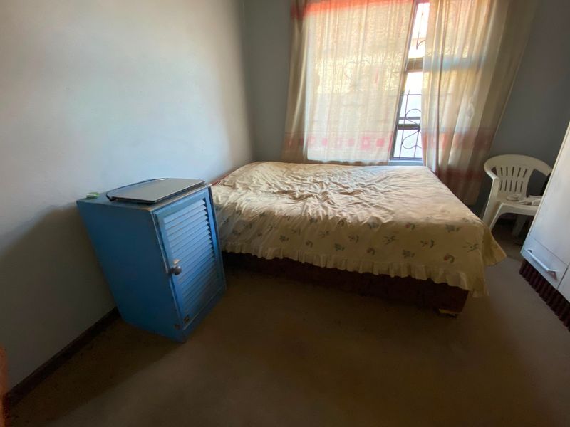A bedroom featuring a window with security bars, requiring cosmetic updates to the flooring and wall finishes to improve its overall appeal.