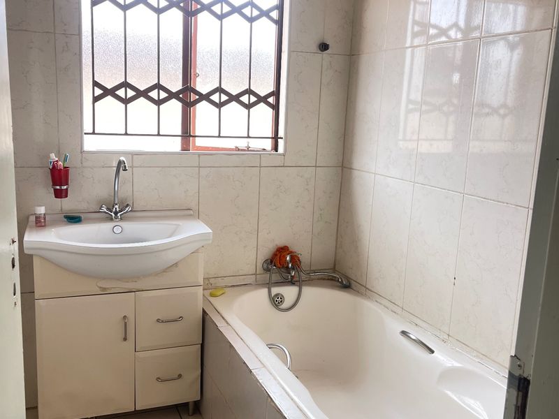 A functional bathroom featuring a built-in bathtub, vanity cabinet with basin, and tiled finishes, requiring some maintenance and cosmetic updates.