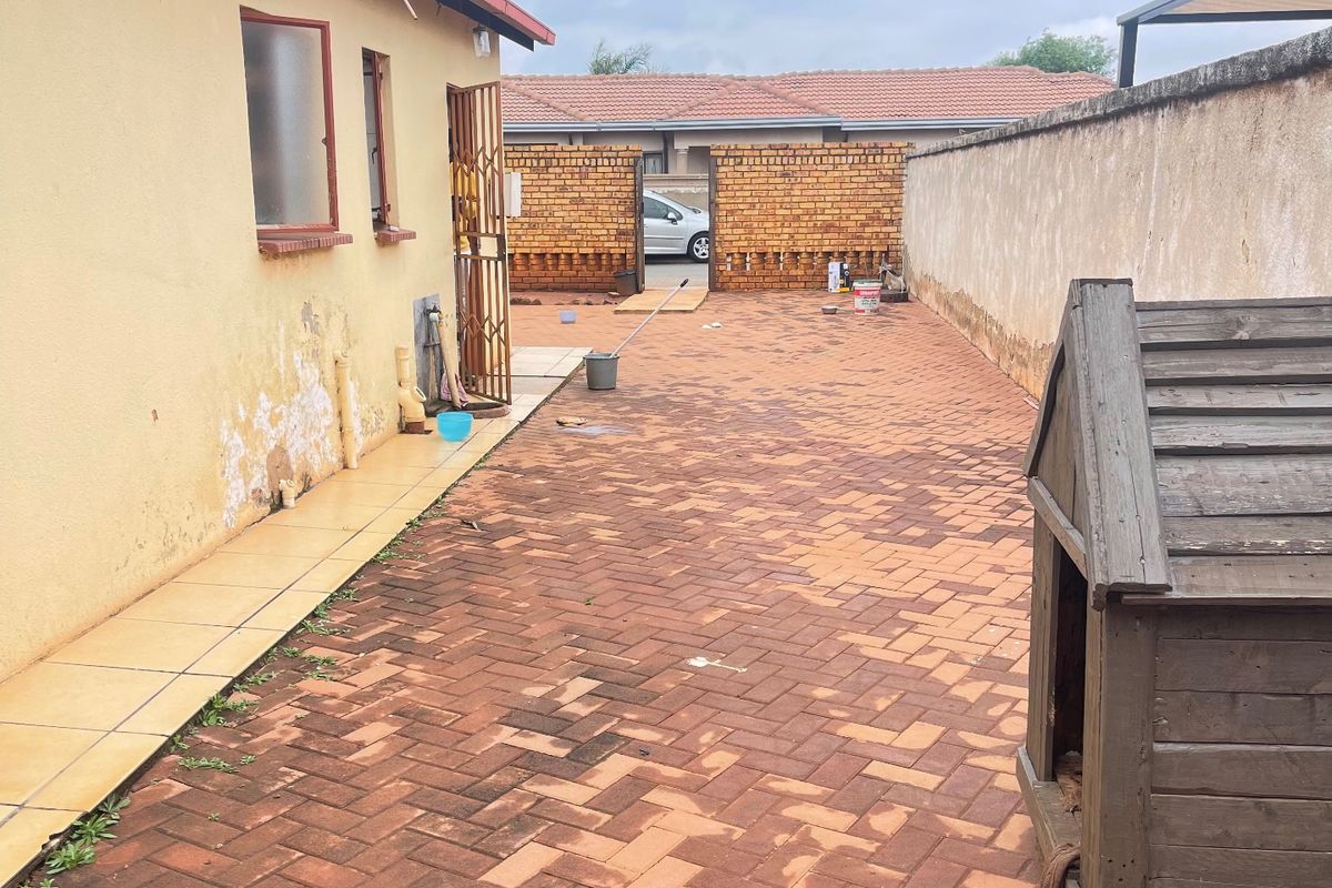 Rear exterior area featuring brick paving, a perimeter wall, and a tiled walkway along the side of the house.
