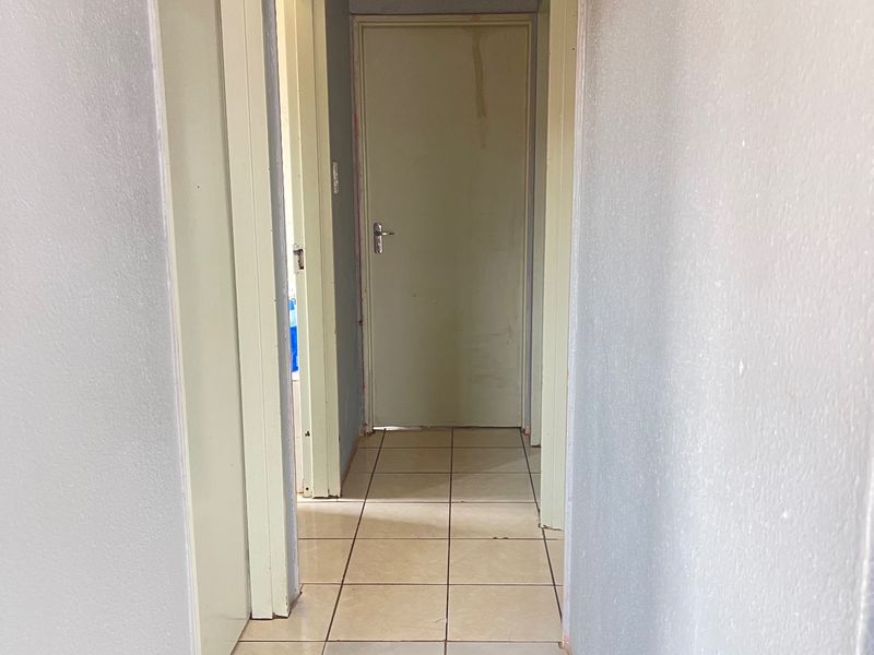 A functional hallway featuring tiled flooring, multiple interior doors, and a ceiling access hatch, requiring minor cosmetic updates to improve its overall appearance.