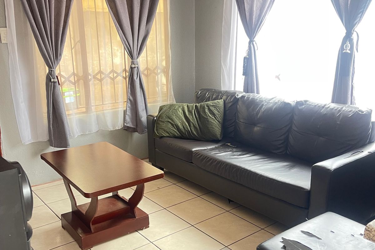 A living room featuring ceramic floor tiles and windows fitted with security bars, offering a functional space with potential for cosmetic updates.