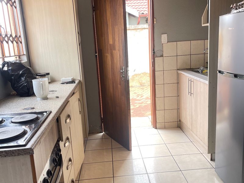 A functional kitchen featuring built-in cabinetry, an electric hob, oven, and tiled finishes, with direct access to the exterior through a wooden door.