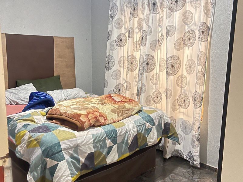 A bedroom featuring tiled flooring and a window with a curtain rail, requiring cosmetic updates to the wall finishes.