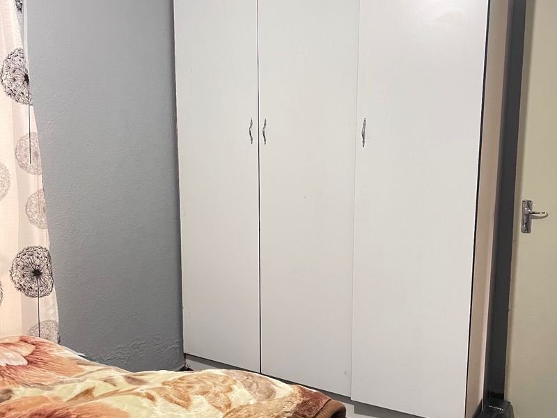 A bedroom featuring a white built-in wardrobe and coving detail, with some visible wear to the wall finish near the floor.