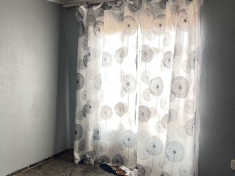 An empty bedroom featuring tiled flooring, a curtain rail, and a simple ceiling light fixture, ready for renovation or staging.