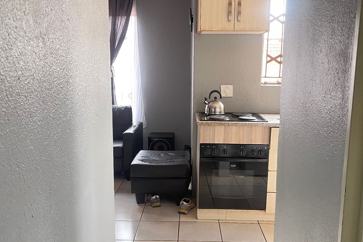 A compact kitchen area featuring built-in cabinetry, an integrated oven and hob, and tiled flooring, viewed from an adjacent hallway.