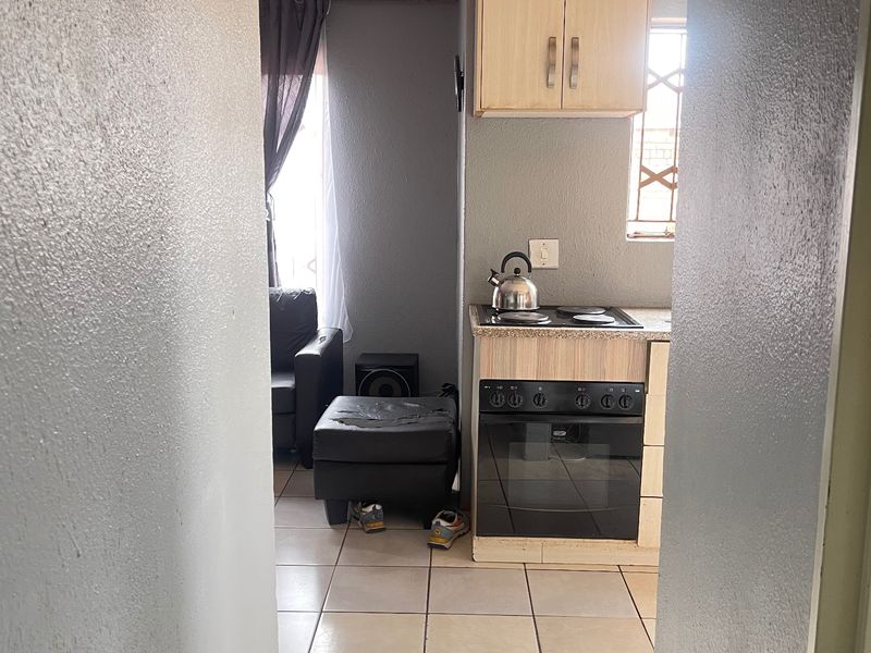 A compact kitchen area featuring built-in cabinetry, an integrated oven and hob, and tiled flooring, viewed from an adjacent hallway.