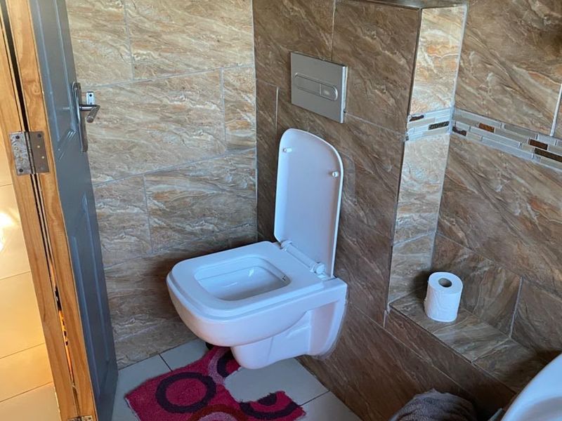 A modern bathroom featuring a wall-mounted toilet with a concealed cistern and decorative brown stone-look wall tiling.