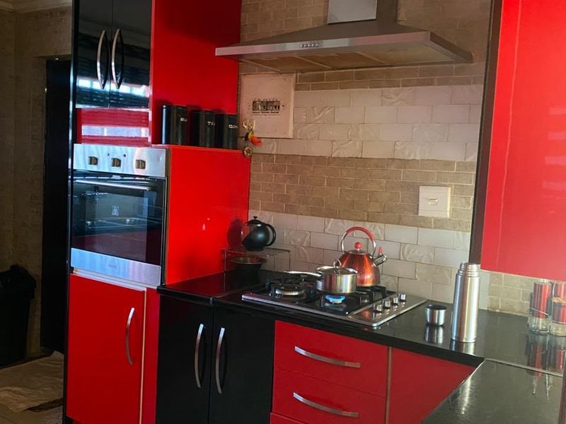 A compact kitchen featuring high-gloss red and black cabinetry, granite countertops, a built-in oven, gas hob, and a tiled backsplash.